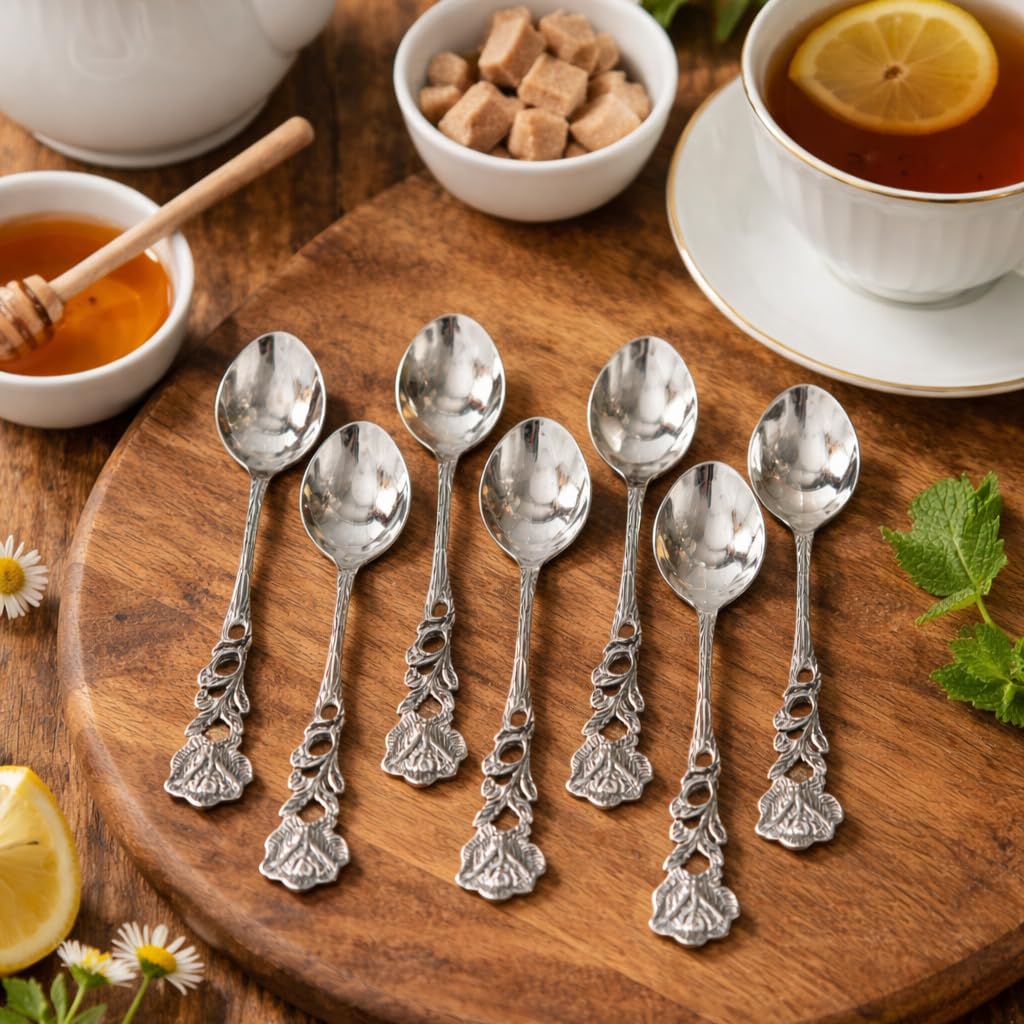 Seven silver rose-handled spoons displayed on a rustic round wooden serving board with honey, lemon slices, and fresh mint leaves.