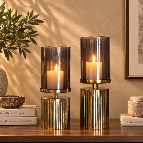 Smoked glass hurricane candle holder set with lit cream pillar candles styled on a luxury wooden console table.