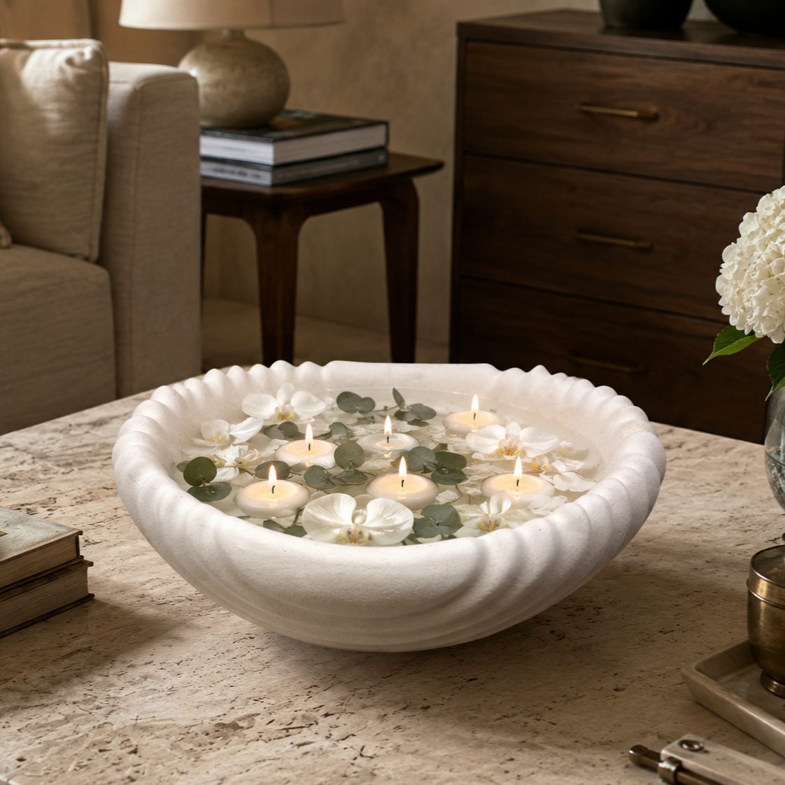 Scalloped white ceramic urli filled with floating candles, white orchids, and eucalyptus leaves, creating an elegant coffee table centerpiece.