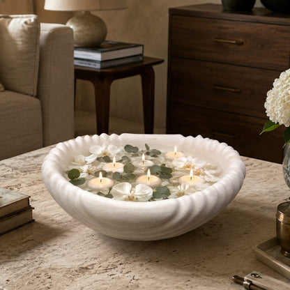 Scalloped white ceramic urli filled with floating candles, white orchids, and eucalyptus leaves, creating an elegant coffee table centerpiece.