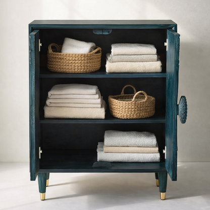 Teal carved wooden cabinet with open doors showcasing spacious storage shelves styled with folded towels and woven baskets.