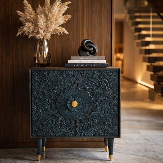 Teal carved wooden storage cabinet with floral detailing styled in a modern hallway with decorative books and sculptural accents.