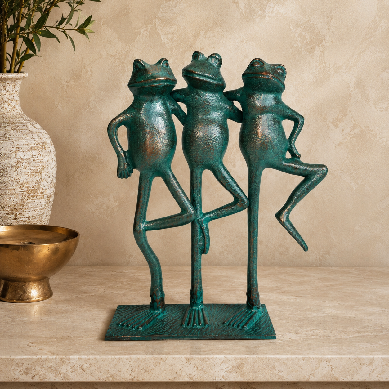Three Frogs decorative metal sculpture with a verdigris finish displayed on a luxury travertine console against a warm beige Venetian plaster wall in a premium modern interior.