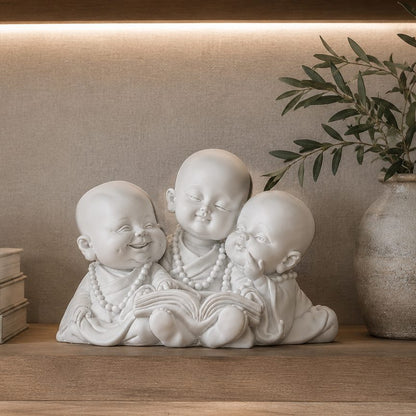 Three Little Monk Reading Figurine in premium white resin displayed on a wooden shelf with decorative books and greenery, luxury home décor accent for living room or office.