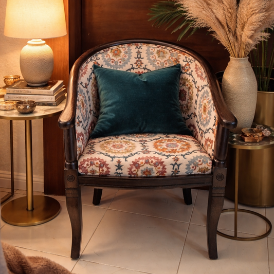 Vintage patterned upholstered accent chair with dark wood frame styled with a deep green velvet cushion, brass side tables, ceramic lamp, stacked books, and decorative vases in a warm cozy interior setting.