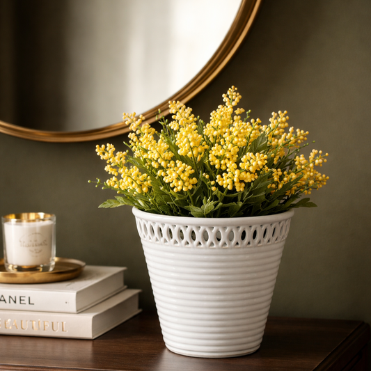 White ceramic ribbed planter with lattice rim holding artificial yellow berry flowers, styled on a dark wood console table with round mirror, books, and candle against a deep olive green wall in a luxury home décor setting.