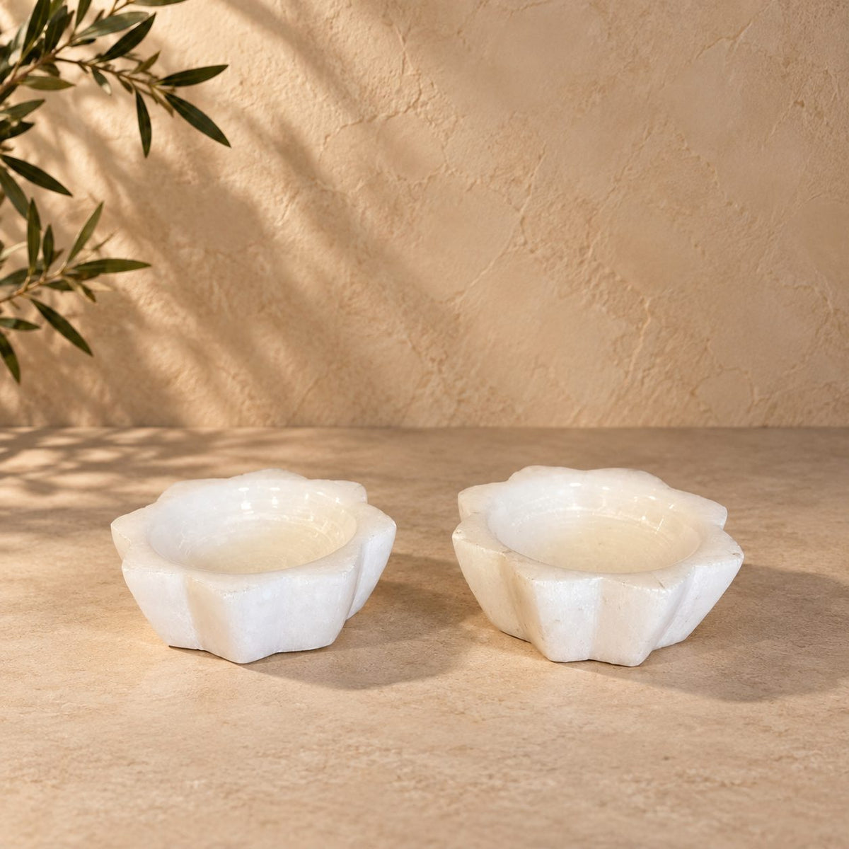 Handcrafted white selenite lotus tea light holder set displayed on a premium beige stone surface with elegant natural lighting.