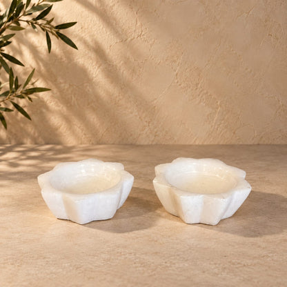 Handcrafted white selenite lotus tea light holder set displayed on a premium beige stone surface with elegant natural lighting.