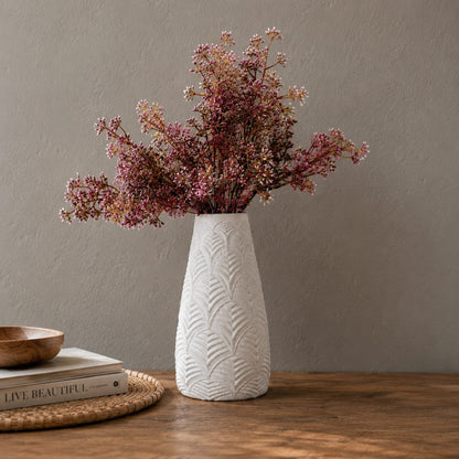 Elegant white textured ceramic vase with embossed leaf detailing and pink floral stems, styled on a wooden tabletop against a soft grey wall for modern luxury home decor.