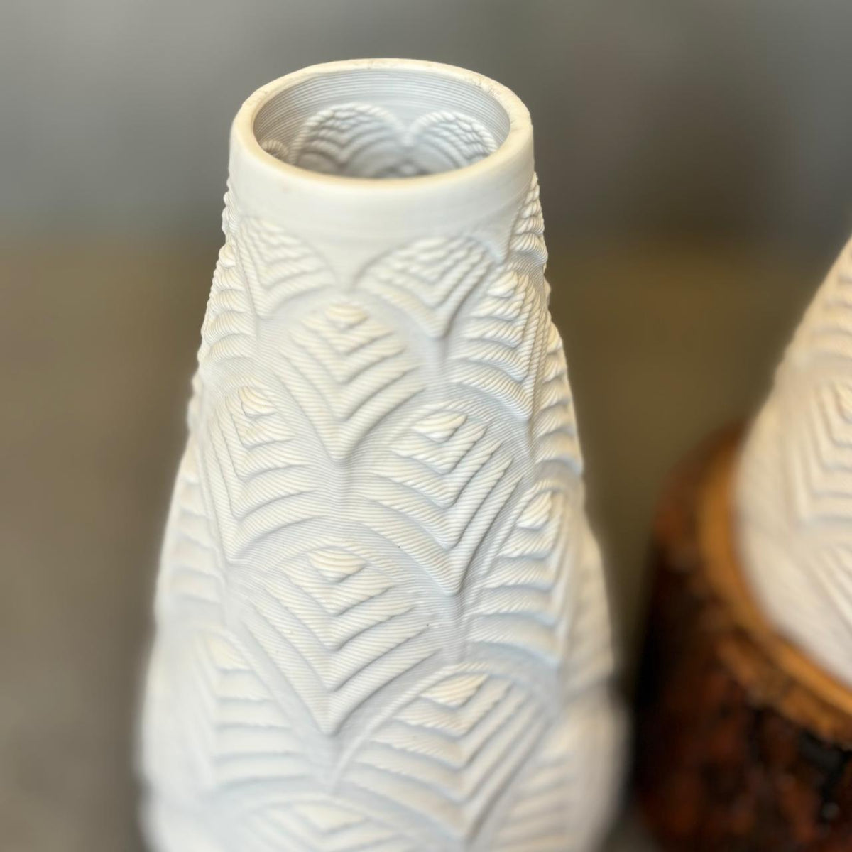 Close-up view of a white textured ceramic vase featuring intricate embossed leaf-inspired detailing and a matte finish in a modern minimalist décor setting.