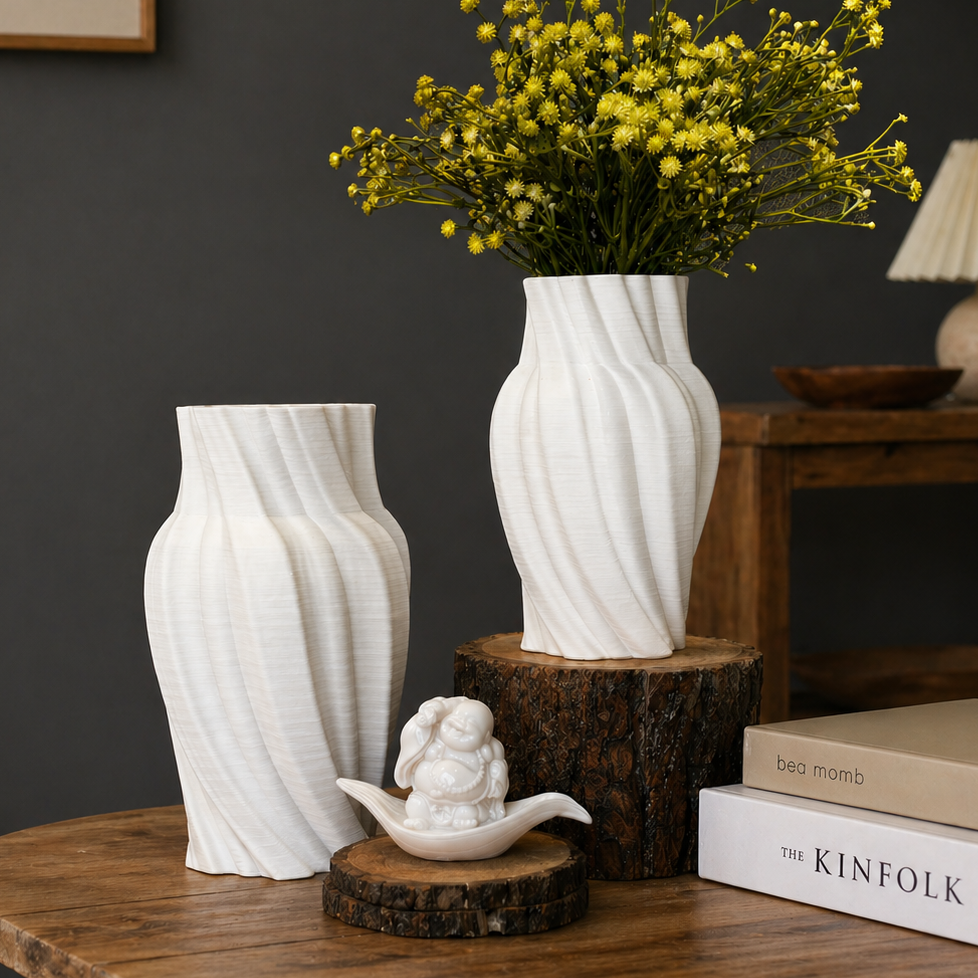 Modern white twist ceramic vases with yellow flowers and decorative figurine on a wooden table against a dark grey wall.