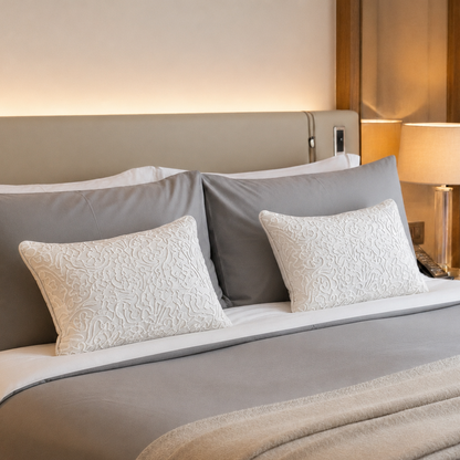 Ivory embroidered lumbar cushion covers styled on a luxury bed with grey bedding, showcasing elegant textured embroidery and premium home décor styling.