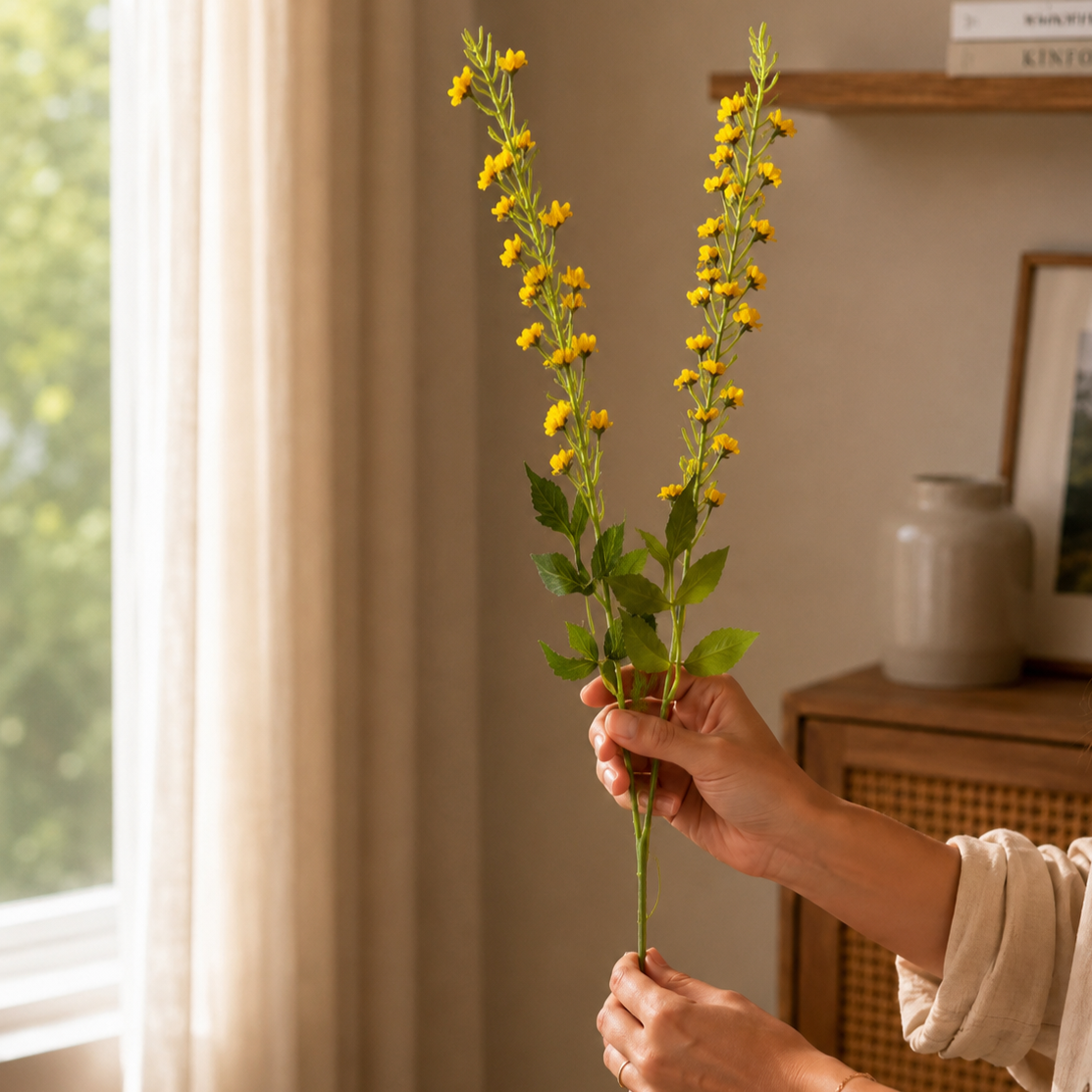 Woman holding yellow artificial flower stems in a warm modern home setting with soft natural light and elegant decor.