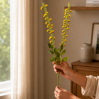 Woman holding yellow artificial flower stems in a warm modern home setting with soft natural light and elegant decor.