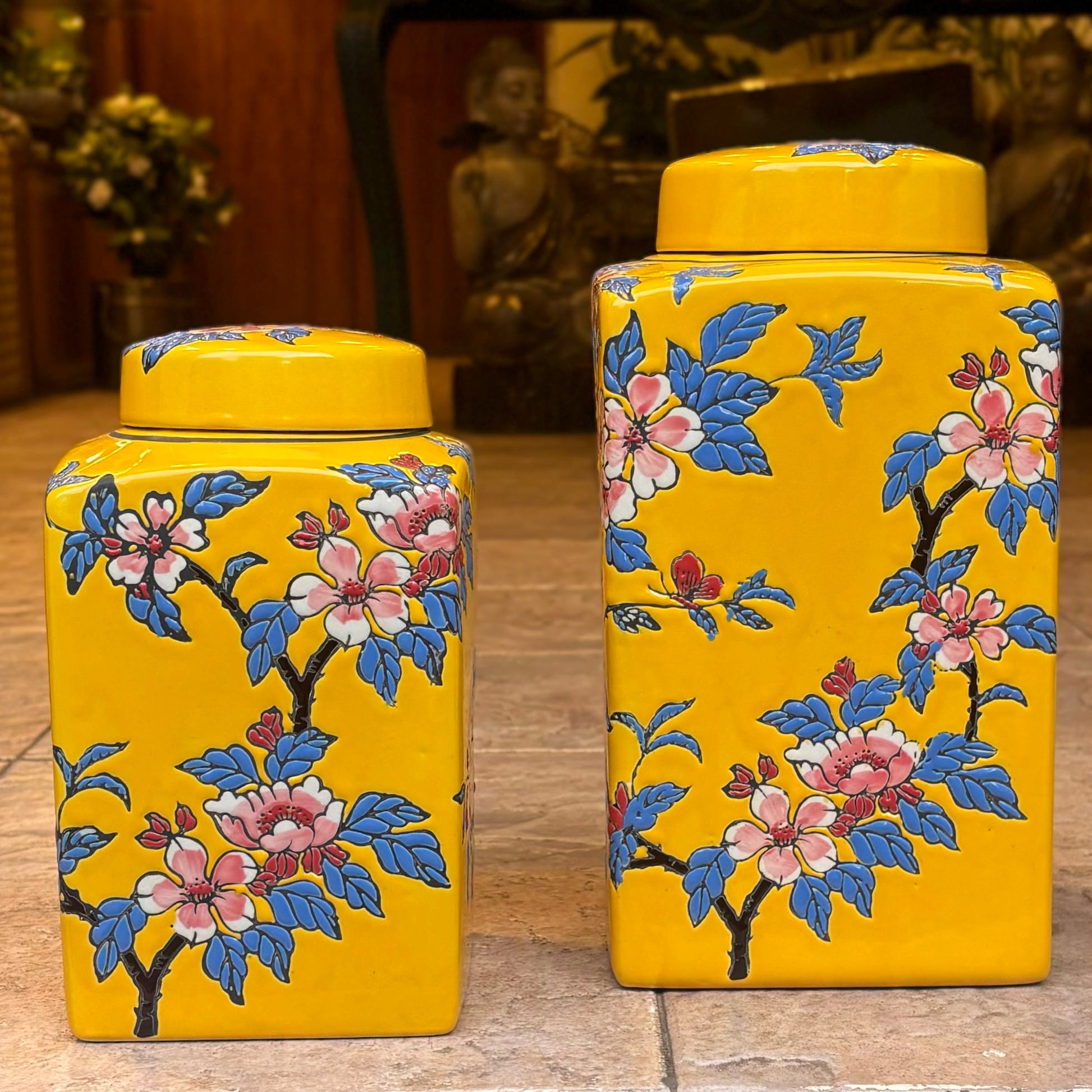 A set of two bright yellow rectangular ceramic ginger jars with hand-painted pink cherry blossoms and blue leaves.