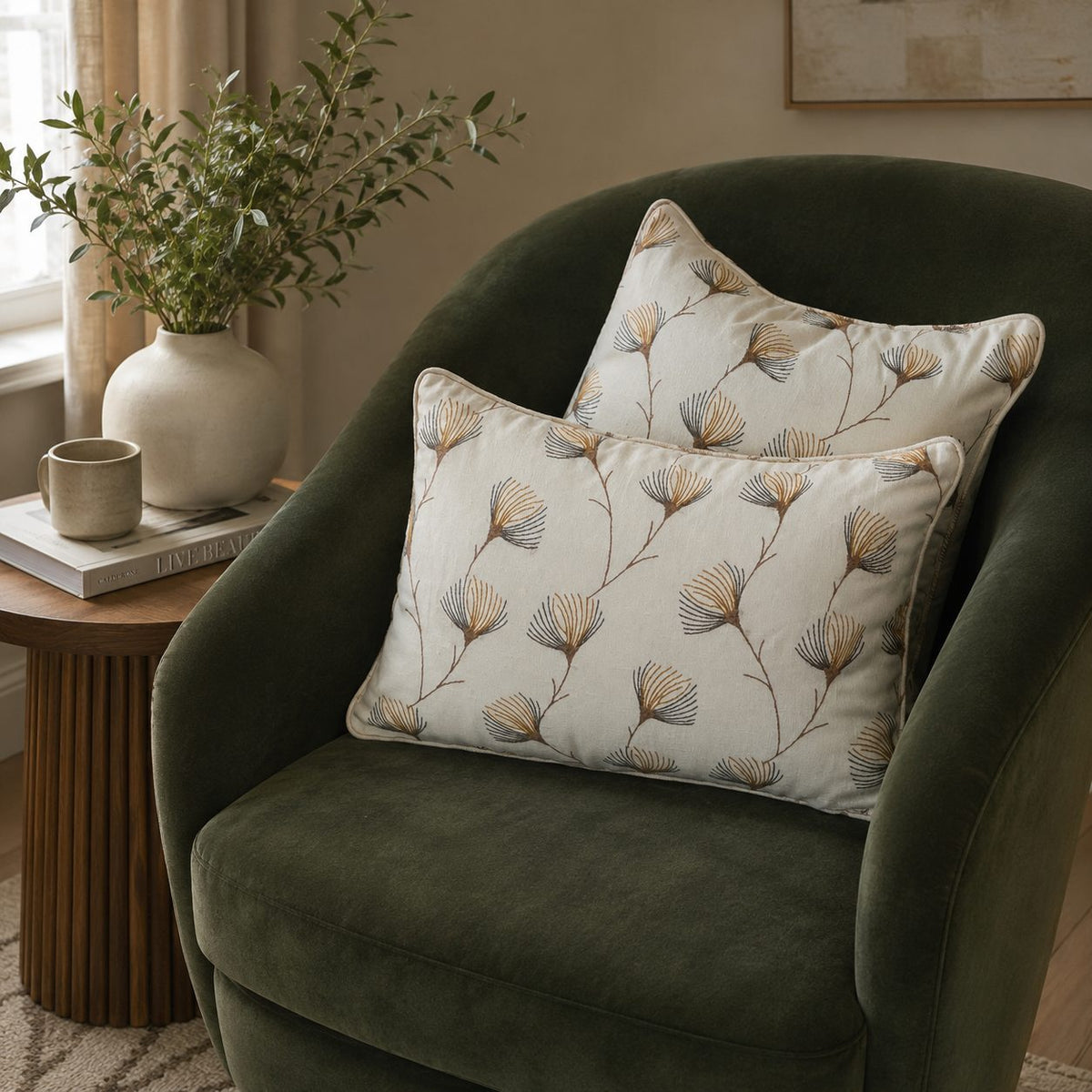 Floral linen cushion covers styled on a dark green velvet accent chair in a modern living room with natural light and elegant home décor accents.