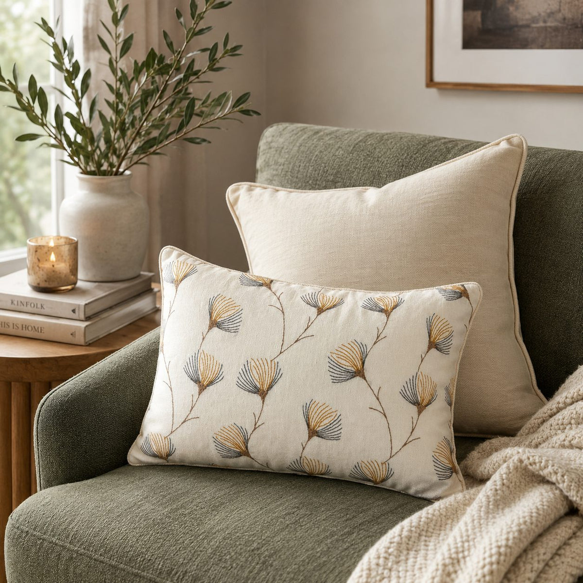 Floral embroidered linen cushion cover styled on a sage green sofa with a neutral cushion, cozy throw blanket, and natural décor in a modern living room setting.
