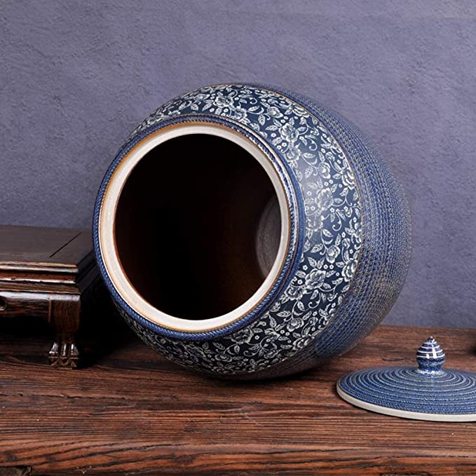 A large, round handcrafted ceramic jar with a blue floral pattern around the neck and a textured base, shown open with the lid resting nearby on a wooden surface.