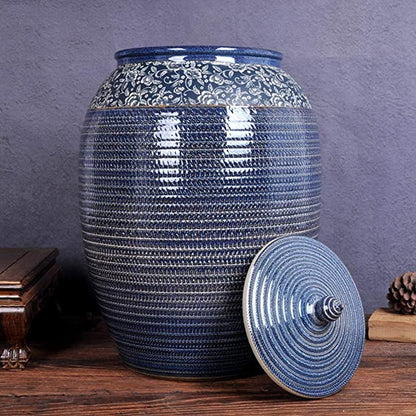 A tall, luxury blue stoneware jar with a white floral vine pattern on the shoulder and a matching conical lid, set against a neutral studio background.
